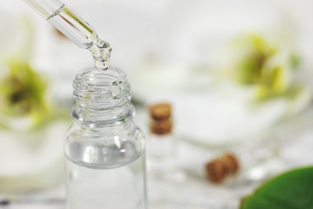 A pipette drops a clear serum into a small glass bottle.