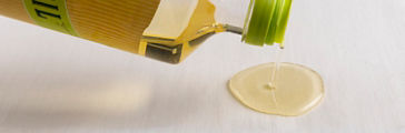 Olive oil pouring from bottle onto white surface