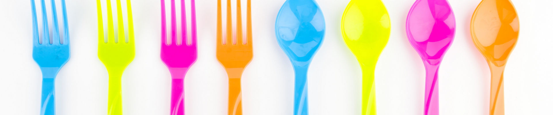 Row of neon-colored spoons and forks laid out on a white background 