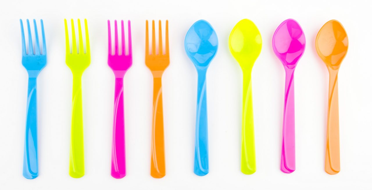 Row of neon-colored spoons and forks laid out on a white background 