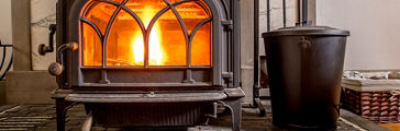 High efficiency cast iron wood stove burning firewood on a custom hearth constructed from black slate and white glass tile. A cast iron tea kettle humidifier sits on top of the stove.; Shutterstock ID 208626310; PO: redownload; Job: redownload; Client: redownload; Other: redownload