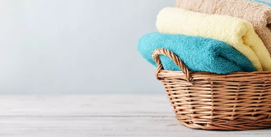 Bath towels of different colors in wicker basket on light background 