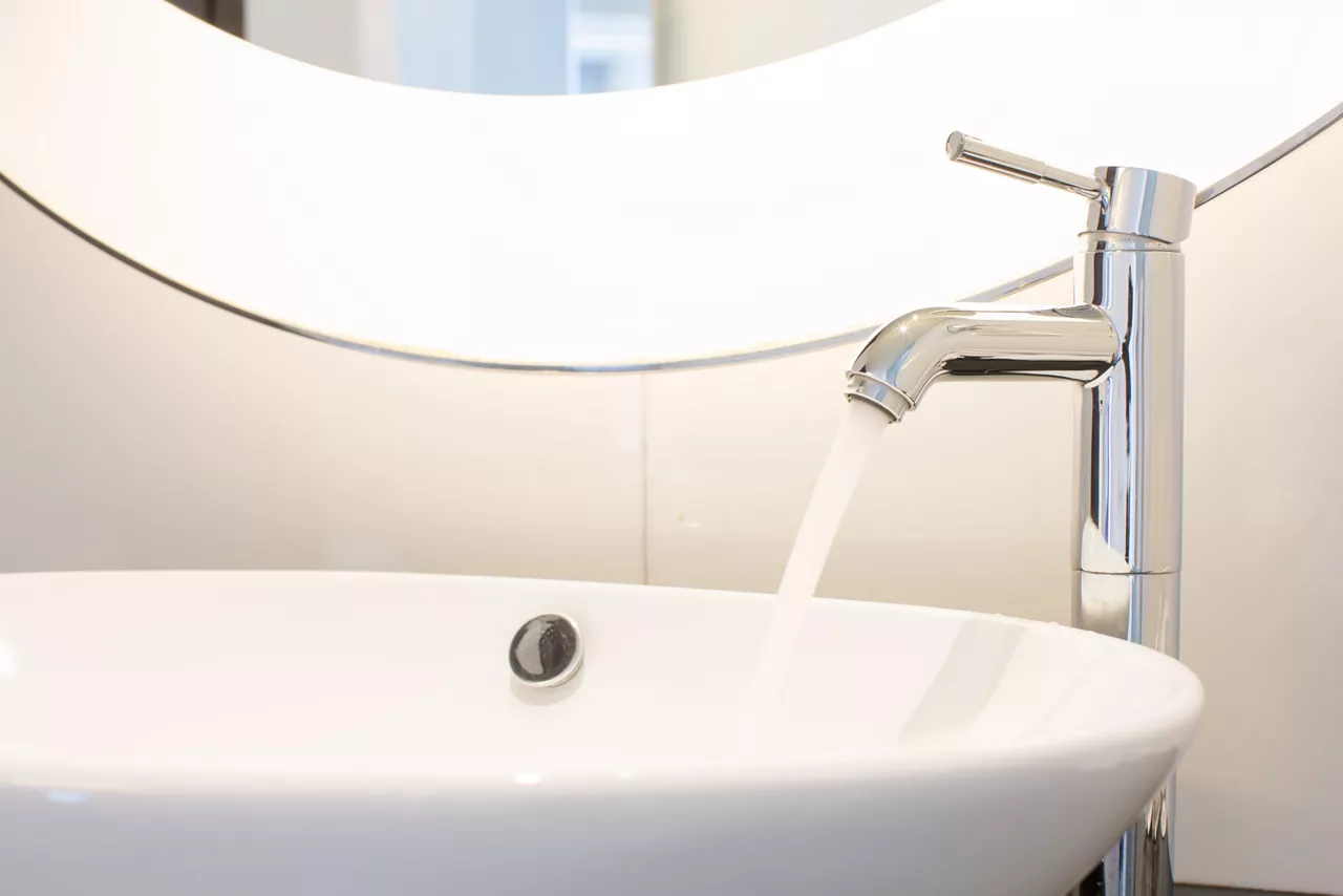 Modern bathroom sink with faucet turned on and mirror sitting above