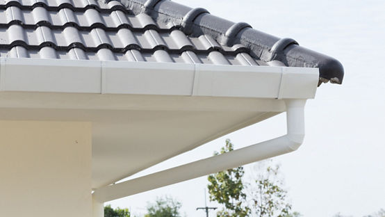 Part of the roof of a house with a white drainpipe and guttering 