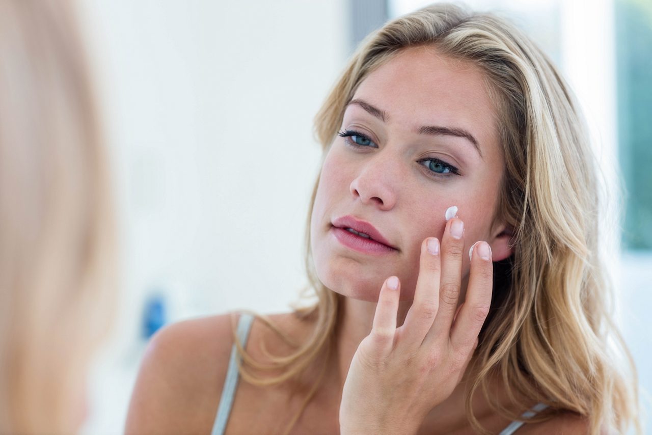 Una hermosa mujer sonriente que se aplica crema en el rostro del baño 