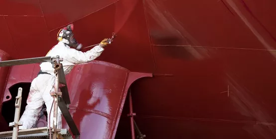 Worker painting ship hull with airbrush paint