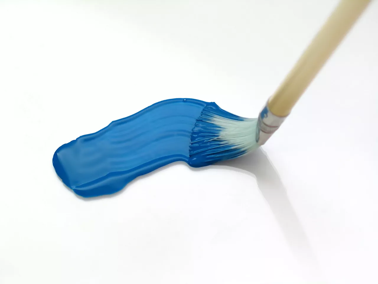 Paint brush smearing blue paint onto a white surface