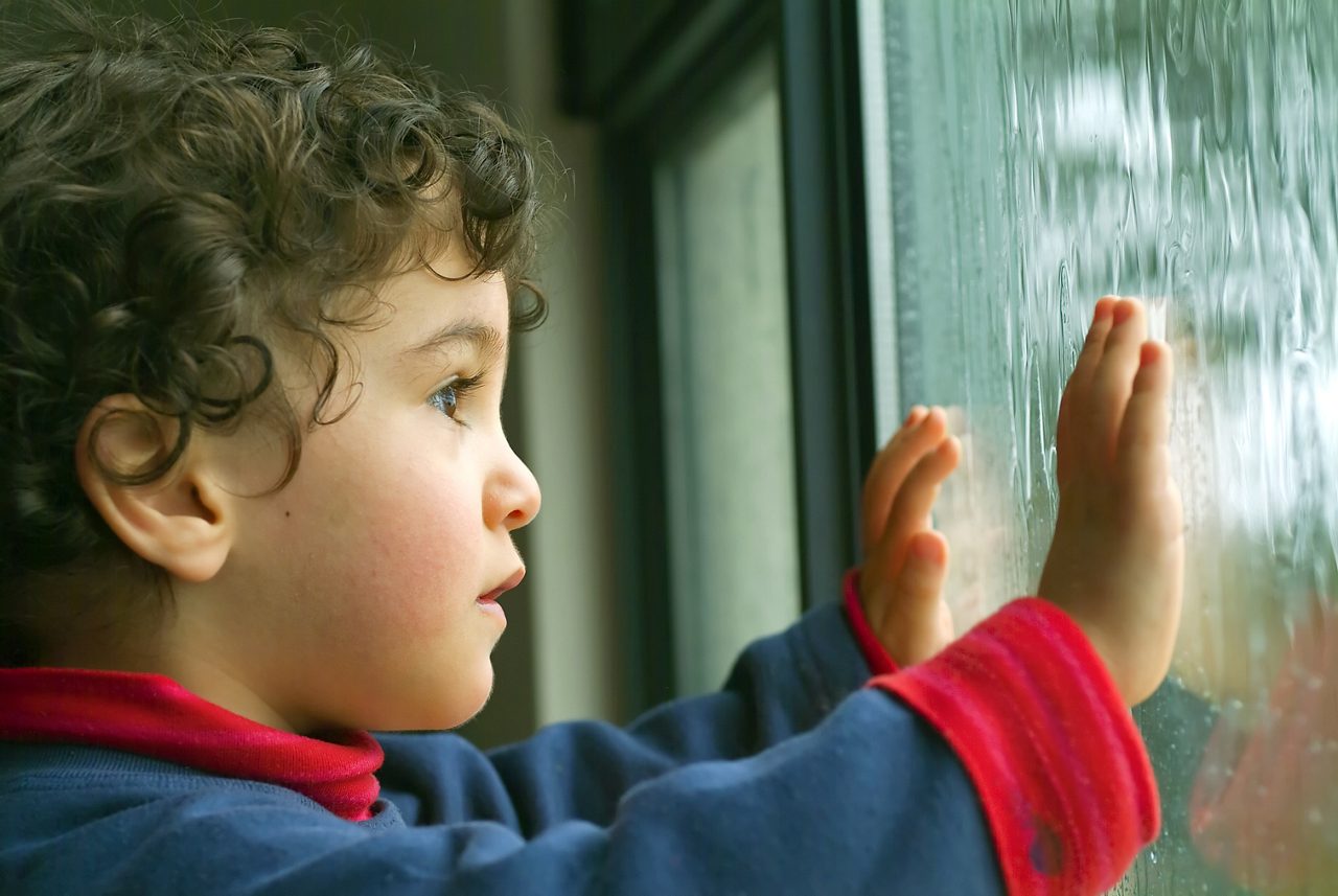 Niño con las manos en la ventana mirando hacia afuera